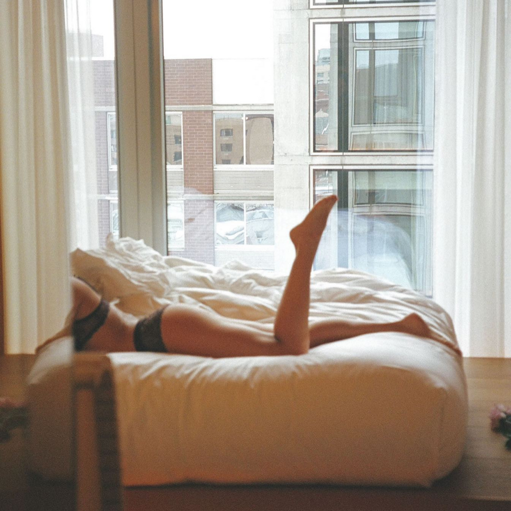person laying in bed by a window wearing comfortable lingerie