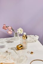 Skincare serum bottle with gold cap on a purple background with flowers and jewelry 
