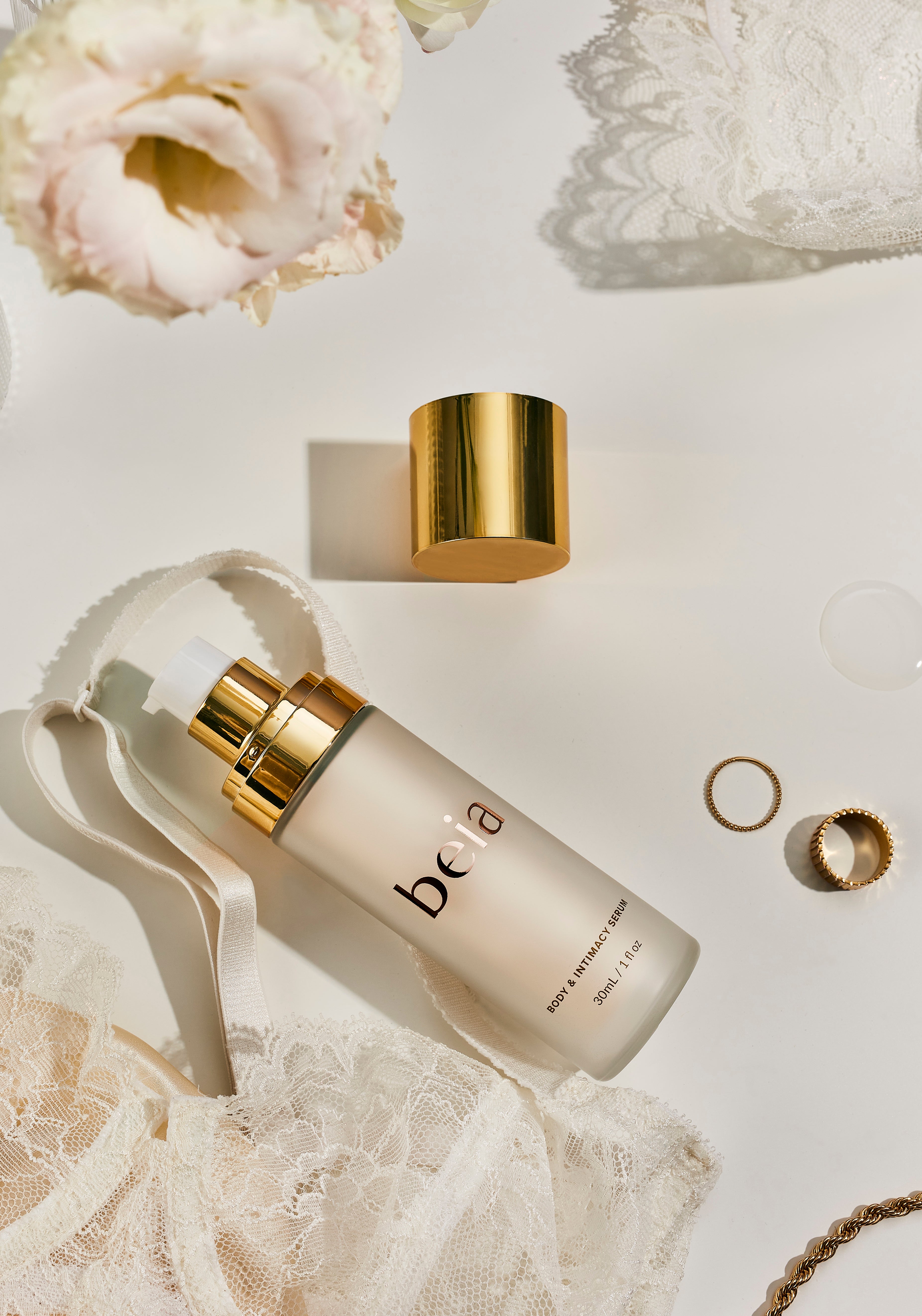 Skincare serum bottle with gold cap on a white background with flowers and jewelry 